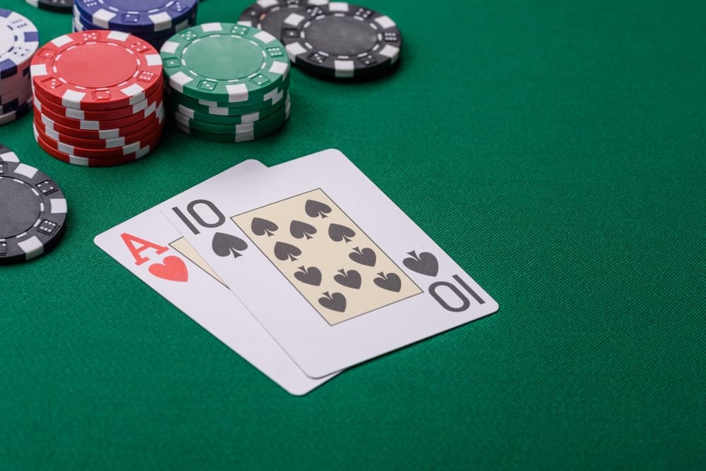 online blackjack auf grünem Spieltisch mit einem Herz-Ass und einer Kreuz-Zehn sowie mehreren Casino-Chips im Hintergrund.